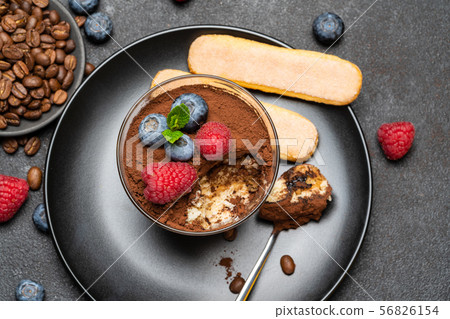 Classic tiramisu dessert portion with blueberries and raspberries in a glass cup on stone serving Classic tiramisu dessert portion with blueberries and raspberries in a glass cup on stone serving 56826154