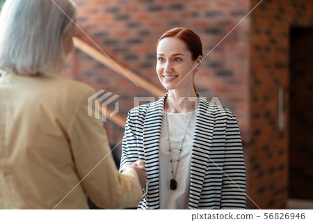 Young red-haired businesswoman shaking hands with her senior colleague 56826946