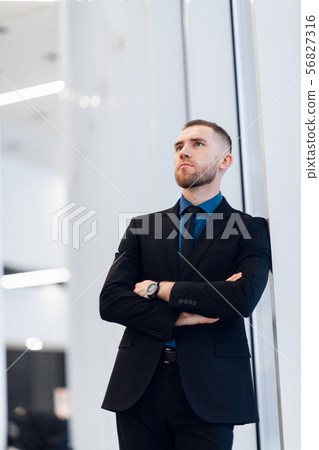 Middle-aged man standing with folded arms leaning against a windowsill turning to look at the camera 56827316
