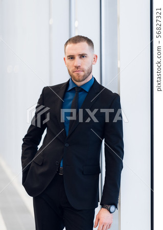 Portrait of handsome man standing in a suit and tie in front of glass door 56827321