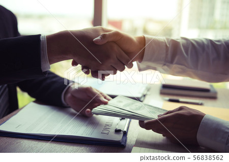 Two corporate businessmen shaking hands while one Two corporate businessmen shaking hands while one 56838562