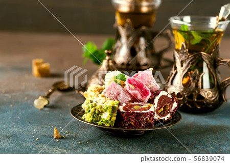 Traditional turkish tea with mint leaves and sweets in a traditional glass on a concrete background Traditional turkish tea with mint leaves and sweets in a traditional glass on a concrete background 56839074