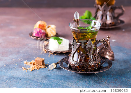 Traditional turkish tea with mint leaves and sweets in a traditional glass on a concrete background Traditional turkish tea with mint leaves and sweets in a traditional glass on a concrete background 56839083