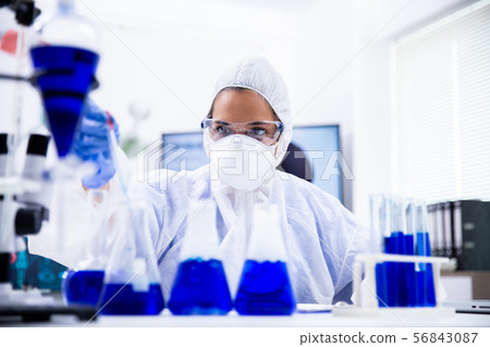 Female scientist in coverall equipment looking at a sample Female scientist in coverall equipment looking at a sample 56843087