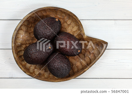 Four whole ripe brown avocados in wooden carved 56847001