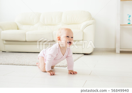 Adorable baby girl learning to crawl in white sunny room. Adorable baby girl learning to crawl in white sunny room. 56849940