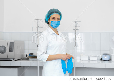 Nurse in scrub and mask puts gloves on her hands Nurse in scrub and mask puts gloves on her hands 56851409