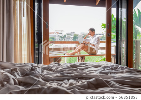 Man working on laptop computer at hotel balcony by the river. 56851855