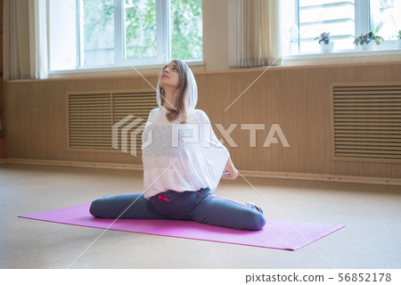 Young slim woman with blonde hair sitting on the yoga mat in dance studio 56852178