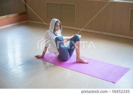 Young slim woman with blonde hair sitting on the yoga mat and stretching her leg Young slim woman with blonde hair sitting on the yoga mat and stretching her leg 56852285