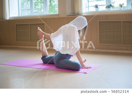 Young slim woman with blonde hair sitting on the yoga mat and doing stretching exercises - pulls the 56852314