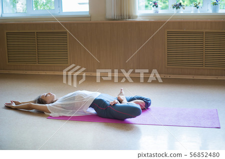 Young acrobatic woman with blonde hair sitting on the yoga mat in lotus pose and leaning back Young acrobatic woman with blonde hair sitting on the yoga mat in lotus pose and leaning back 56852480