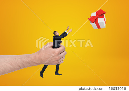 Big male hand holding businessman reaching out to gift box on yellow background 56853036