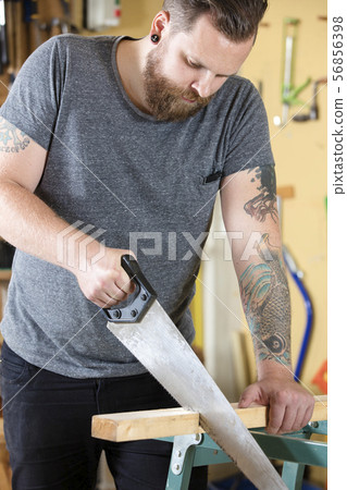 Craftsman sawing wood with hand saw in workshop 56856398