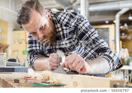 Focused carpenter work with plane on wood plank in workshop 56856797