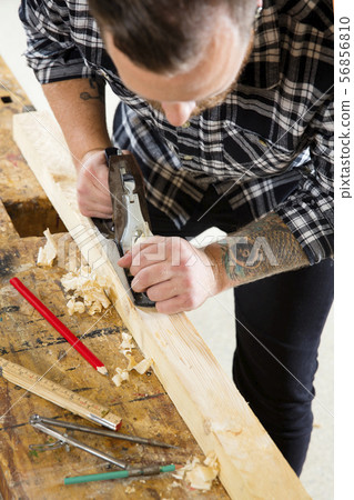Focused craftsman working with plane on wood plank in workshop 56856810