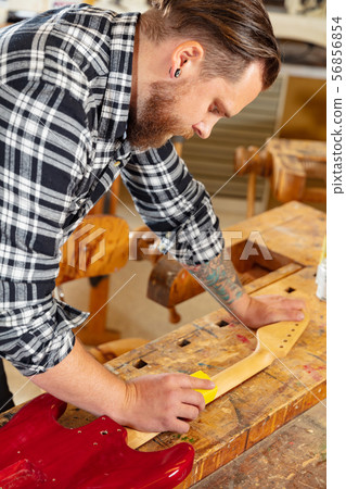 Close-up of craftsman sanding a guitar neck in wood at workshop 56856854