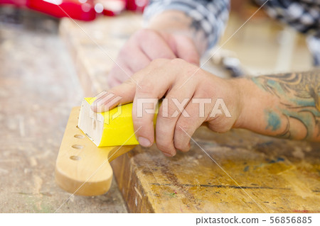 Carpenter sanding a guitar neck in wood at workshop 56856885