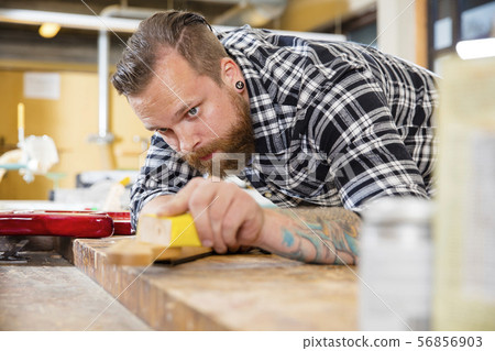 Carpenter sanding guitar neck in wood at workshop 56856903