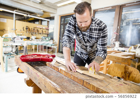 Carpenter sanding a wooden guitar neck in workshop 56856922