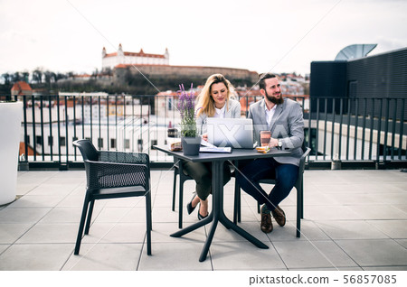 Two young business people with laptop sitting on a terrace outside office, working. Two young business people with laptop sitting on a terrace outside office, working. 56857085