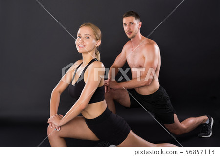 Athletic young couple doing stretching legs exercises together on the black background. 56857113