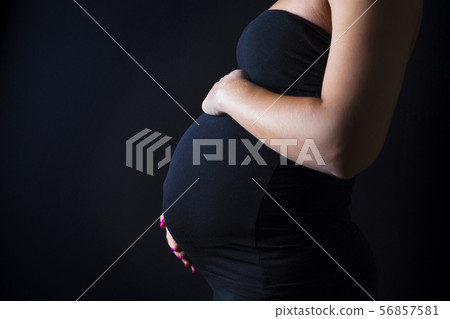 Pregnant woman stands with her hands at the belly Pregnant woman stands with her hands at the belly 56857581