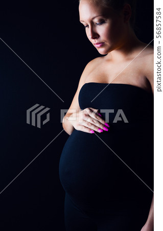 Thoughtful pregnant woman standing with one hand on the belly Thoughtful pregnant woman standing with one hand on the belly 56857584