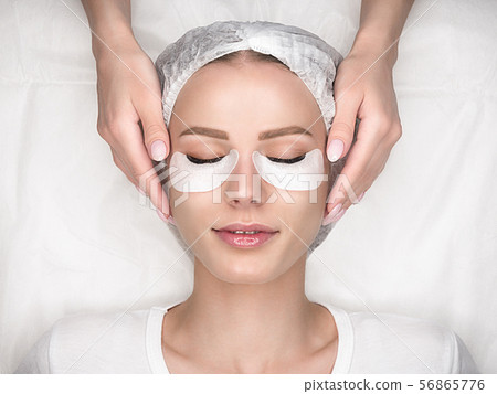 Eyelash extension procedure. Female face with long lashes and cotton patches on lower eyelids. Top 56865776