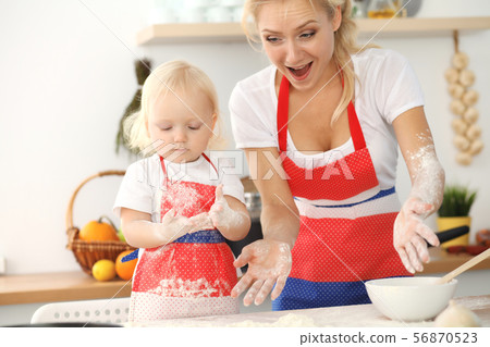 Little girl and her blonde mom in red aprons playing and laughing while kneading the dough in Little girl and her blonde mom in red aprons playing and laughing while kneading the dough in 56870523