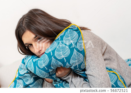 pensive young woman with pillow sitting on bed 56872521