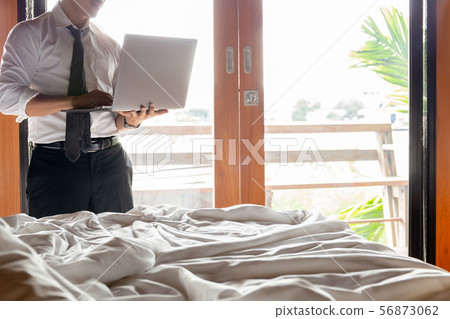 Businessman working with laptop in hotel bed room with sunlight in background. Businessman working with laptop in hotel bed room with sunlight in background. 56873062