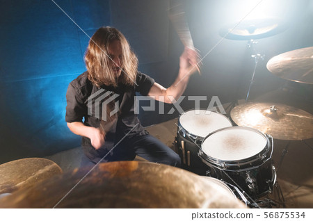 Portrait of a long-haired drummer with chopsticks in his hands sitting behind a drum set. Low key Portrait of a long-haired drummer with chopsticks in his hands sitting behind a drum set. Low key 56875534