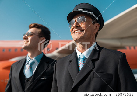Smiling mature men in uniform are ready for flight in airport Smiling mature men in uniform are ready for flight in airport 56875535