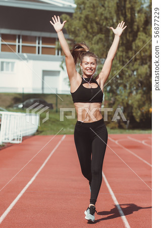 Happy woman with earphones running on racetrack 56877229