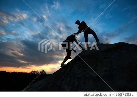 Young man and woman in the mountains. Woman with a rope engaged in rock climbing with man helping 56878023