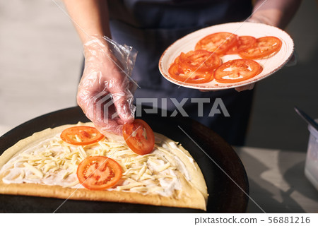 Chef keeping plate with cutted tomato. Woman hand putting tomato slices on pancake lubricated with Chef keeping plate with cutted tomato. Woman hand putting tomato slices on pancake lubricated with 56881216