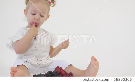 Baby girl in white clothes eats juicy berries on light background Baby girl in white clothes eats juicy berries on light background 56890306