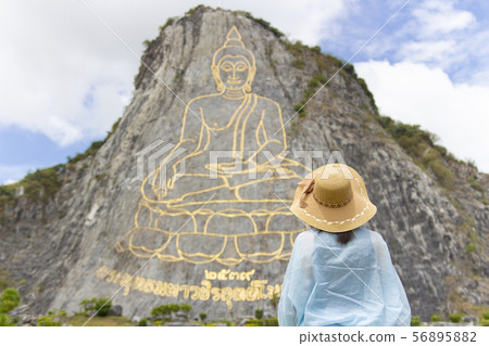 CHONBURI,THAILAND, 29 JULY 2018 :Beautiful young aisan woman is standing on the background of mountain with golden statue of buddha on a hillside at pattaya. 56895882