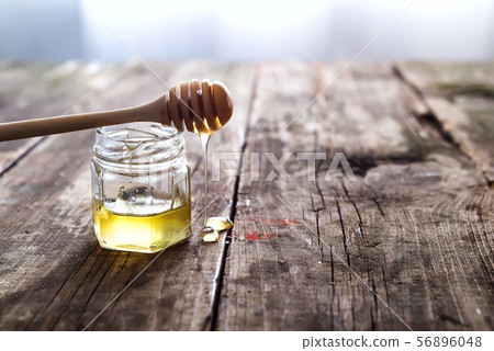 Honey dripping from a wooden honey dipper in a jar on wooden grey rustic background 56896048
