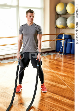 Fitness trainer man aggressive during shading with ropes in a bright fitness room for fitness. Sport 56896092