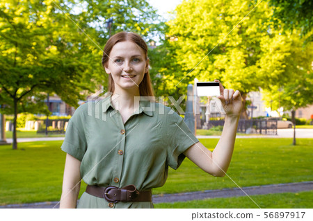 Blonde girl in a summer green dress with a plastic card in a park outdoors. Blonde girl in a summer green dress with a plastic card in a park outdoors. 56897917