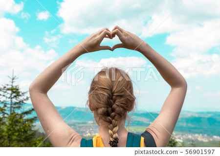 Female hand forms a love hand with a blurred background of mountain and sky Female hand forms a love hand with a blurred background of mountain and sky 56901597
