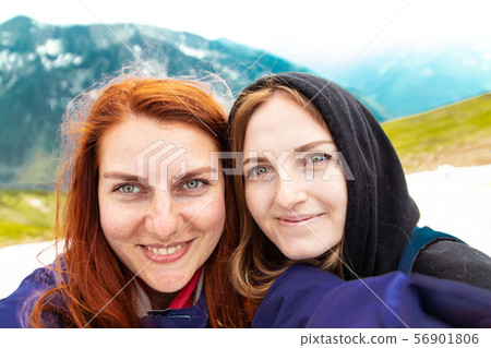 Two girls take a picture with their mobile. Two friends enjoy nature and the outdoors on the side of Two girls take a picture with their mobile. Two friends enjoy nature and the outdoors on the side of 56901806