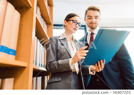 Lawyers in library of law firm discussing strategy in a case holding file 56907203