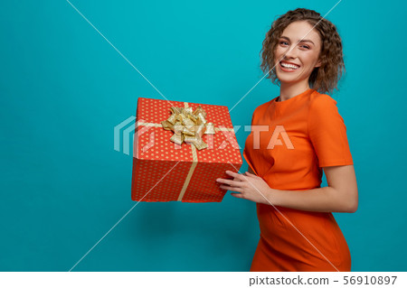 Female in orange dress posing and keeping big present Female in orange dress posing and keeping big present 56910897