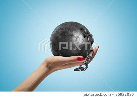 Side closeup of woman's hand facing up and holding black ball and chain on light blue gradient Side closeup of woman's hand facing up and holding black ball and chain on light blue gradient 56922050