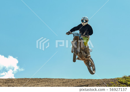 Racer on motorcycle dirtbike motocross cross-country in flight, jumps and takes off on springboard Racer on motorcycle dirtbike motocross cross-country in flight, jumps and takes off on springboard 56927137