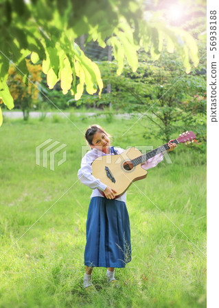 Asian school girl playing the guitar on the lawn , 56938188