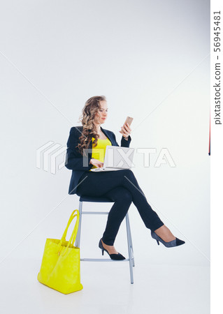 office concept, business plan, fashion-businesswoman in black and yellow suit talking on the phone and working on a laptop. big yellow bag. Beautiful woman sitting on chair on white background 56945481